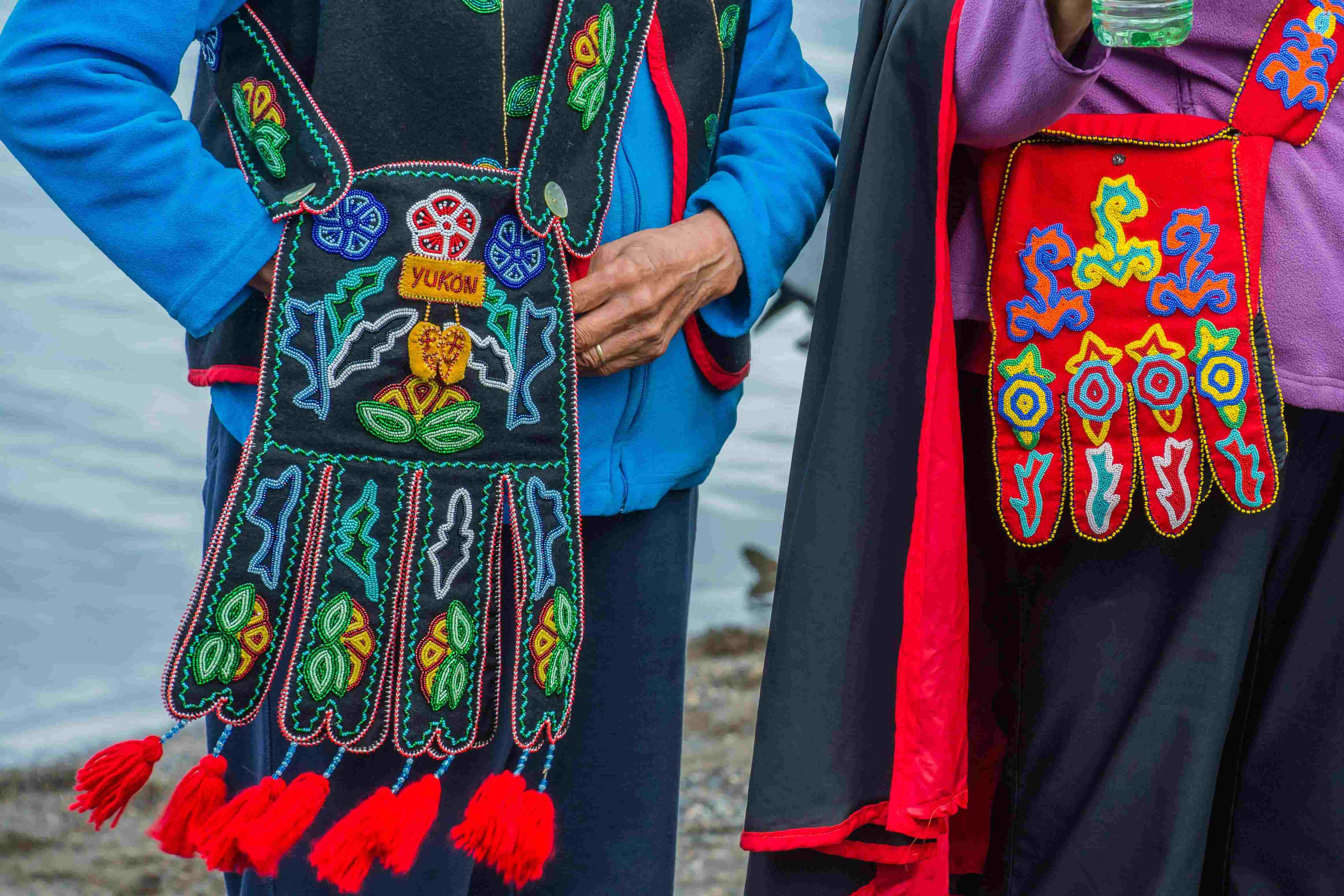 Two people stand by a lake with beautifully beaded bags.