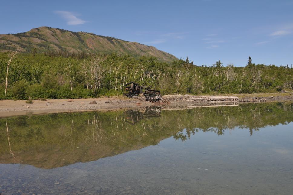 a lake with a mountain in the background and the crumbling remains of a mine artifact