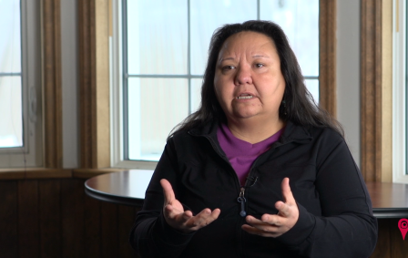 Indigenous woman wearing black full zipper sweater and purple shirt underneath.
