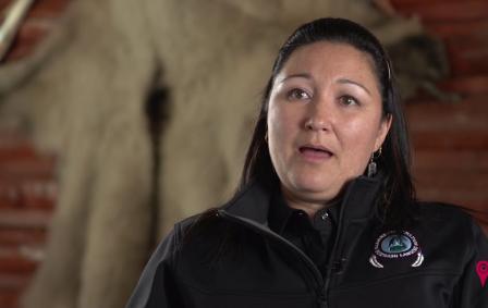 Indigenous woman wearing silver earrings and black vest with Kluane First Nation logo