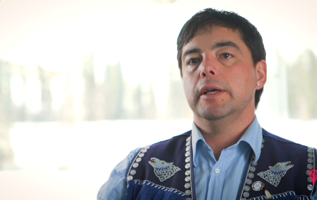 Indigenous man wearing navy blue vest with buttons and beading