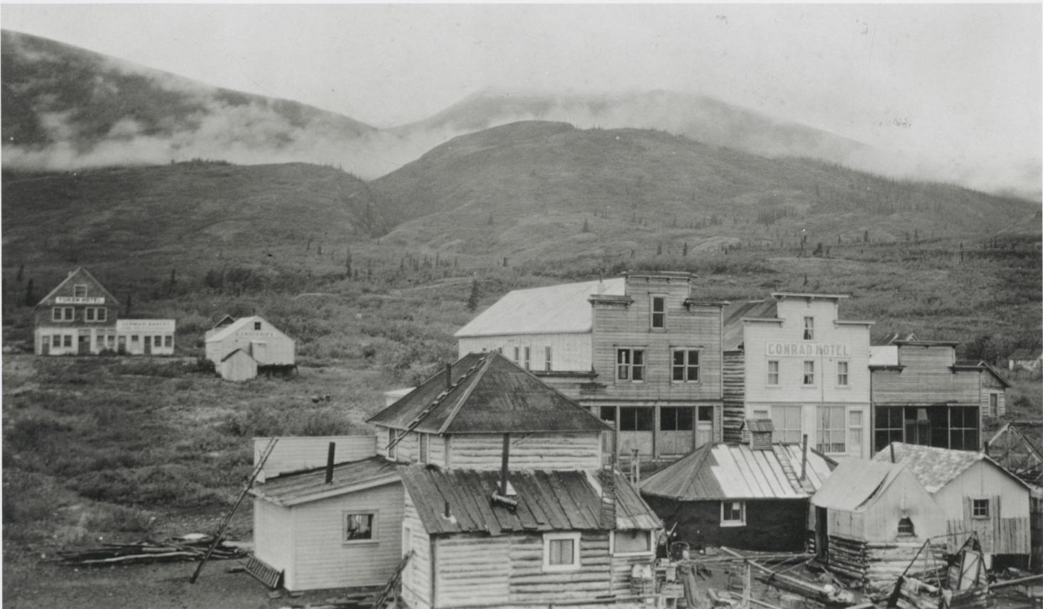 black and white photo of historic buildings with mountains in the background